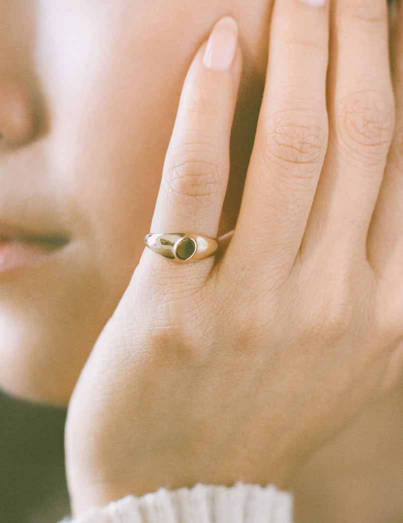 Close-up of a person wearing a dainty gold signet ring on their pinky