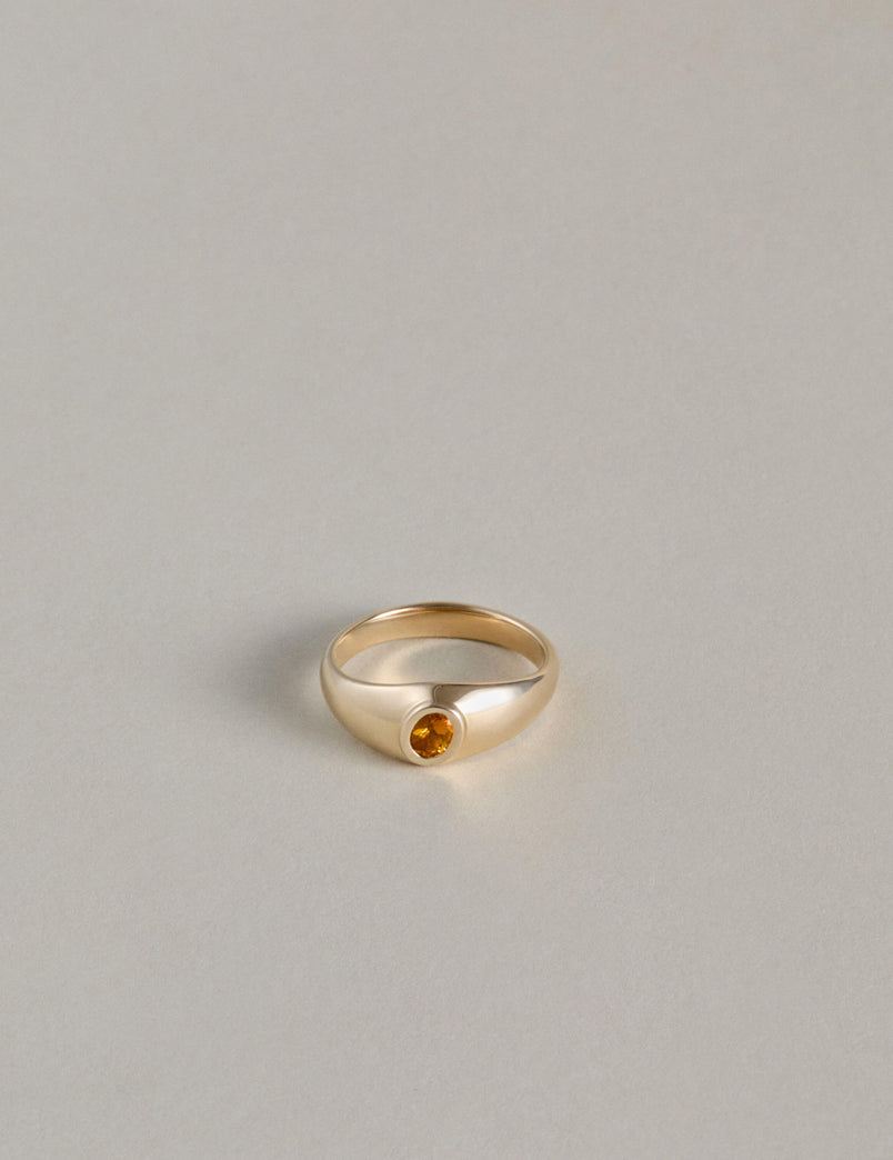 Gold signet ring with an oval citrine gemstone on a light gray background