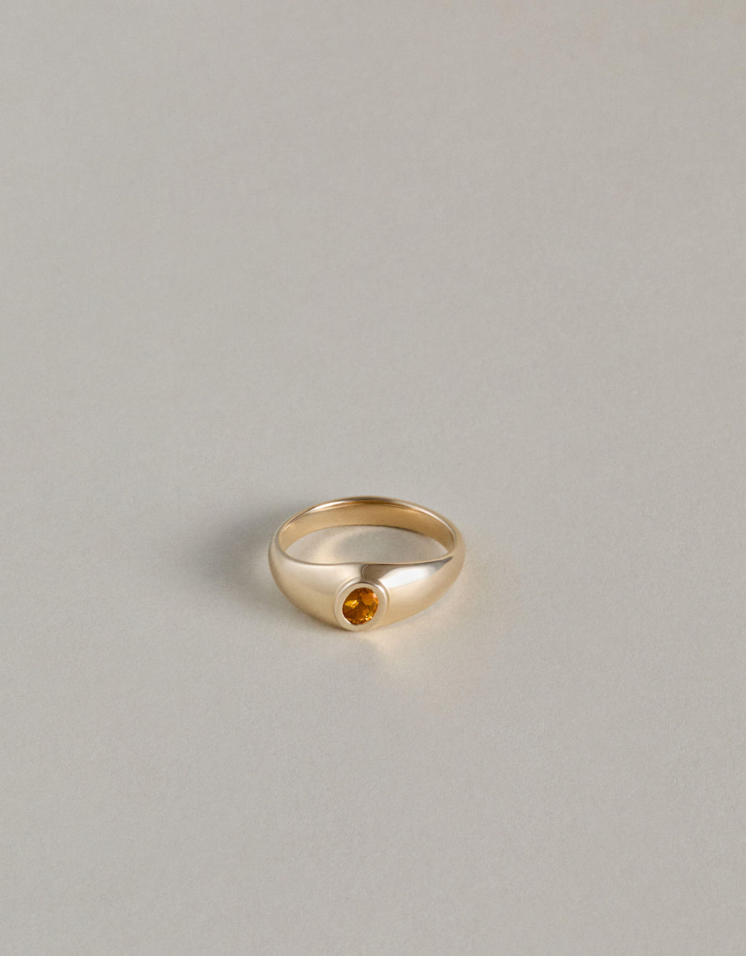 Gold signet ring with an oval citrine gemstone on a light gray background