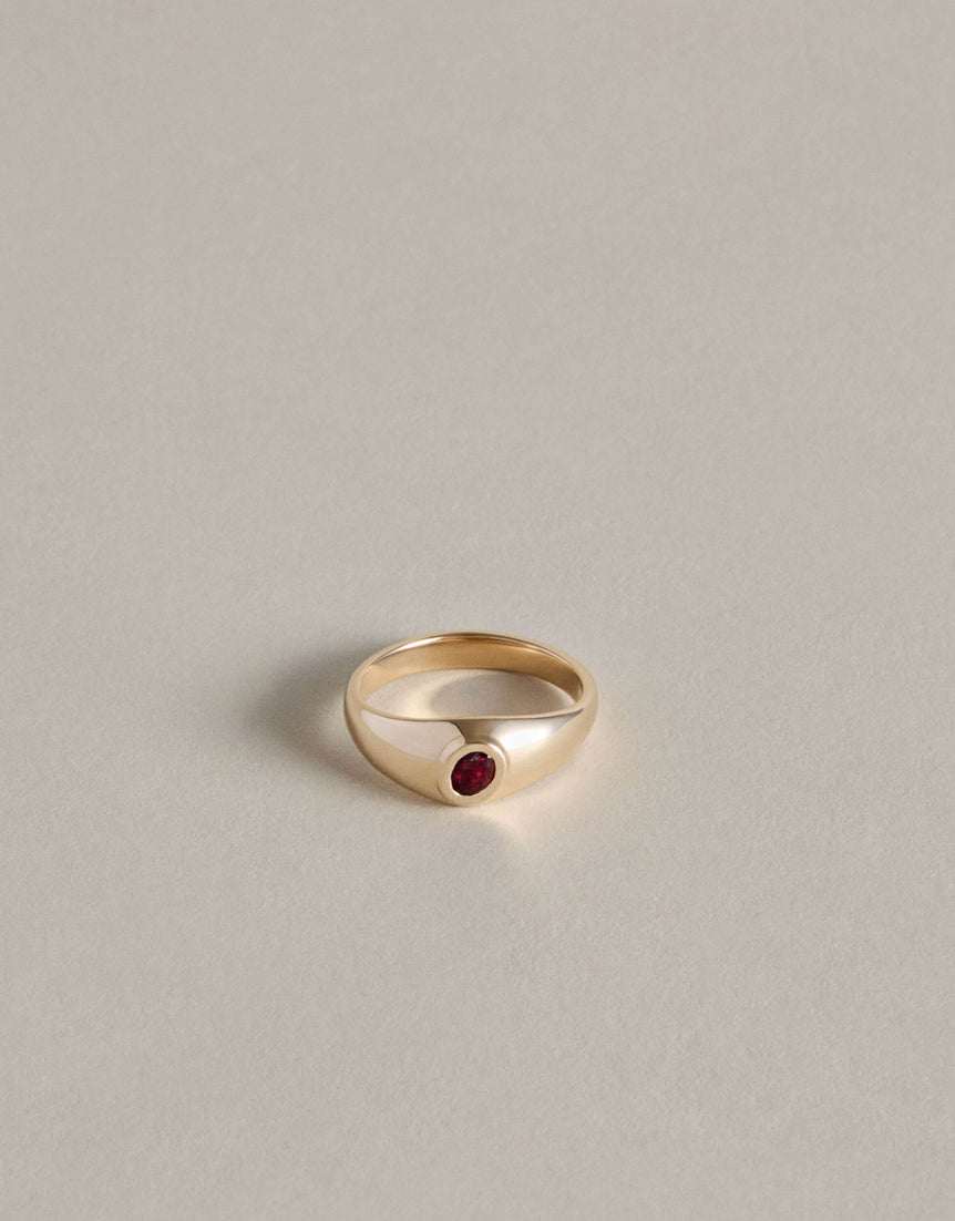 Gold signet ring with an oval garnet on a light gray background