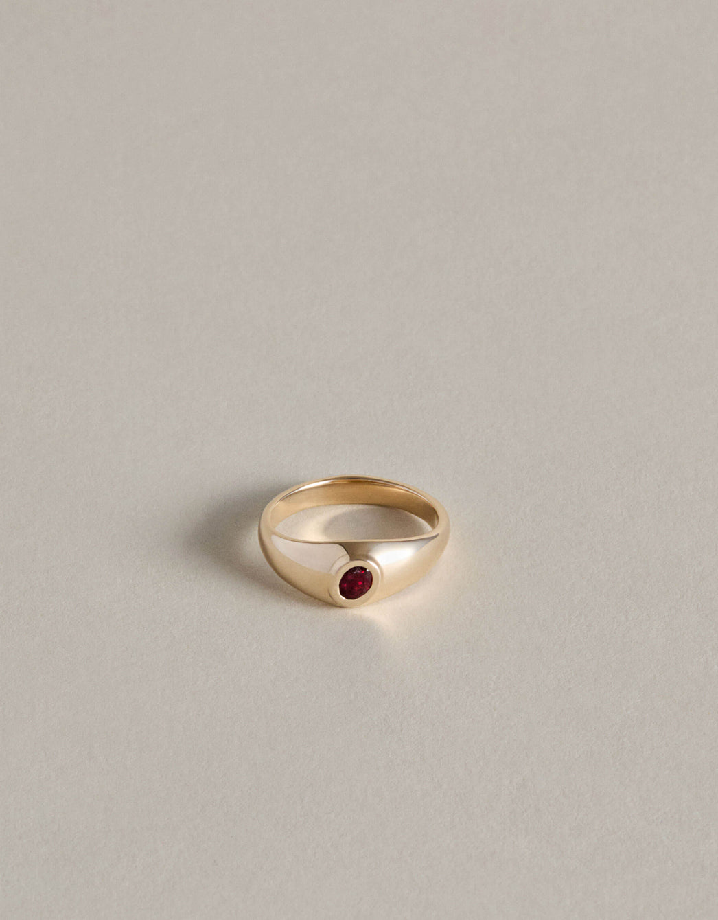 Gold signet ring with an oval garnet on a light gray background