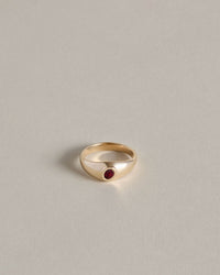 Gold signet ring with an oval garnet on a light gray background