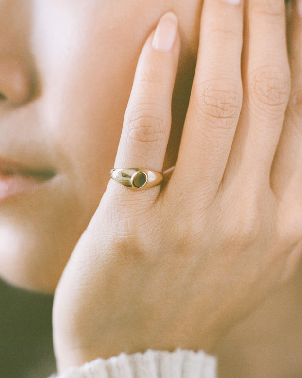 Close-up of a person wearing a dainty gold signet ring on their pinky