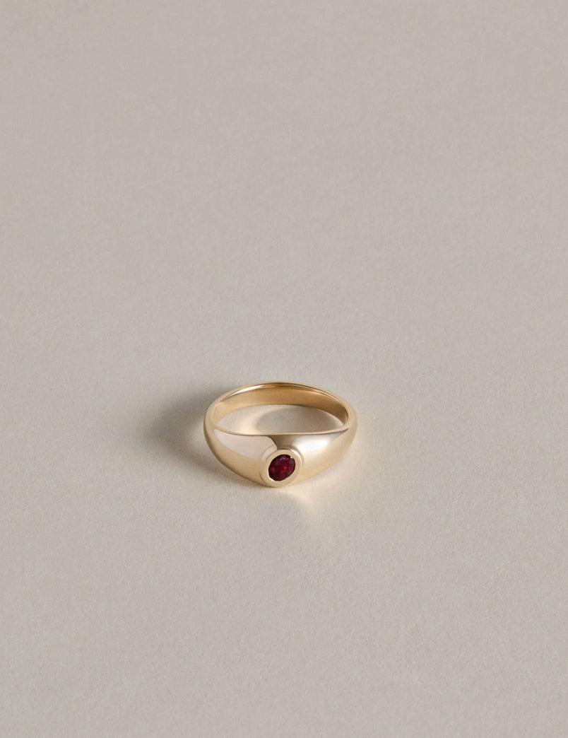 Gold signet ring with an oval garnet on a light gray background